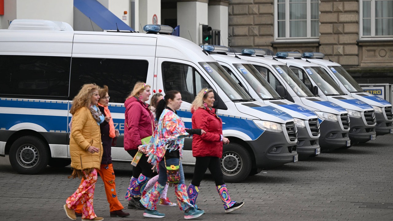 Karnevalisten gehen in ihren Kostümen an Polizeiautos beim Düsseldorfer Rathaus vorbei