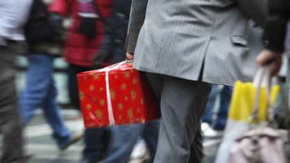 Mann im Anzug mit Geschenk in der Hand geht durch Menschenmenge, Bewegungsunschärfe vermittelt Hektik