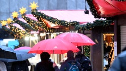 Menschen laufen mit Regenschirm über den Weihnachtsmarkt