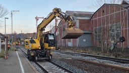 Ein Bagger steht im Gleisbett an einem Bahnhof, die Schienen sind noch unterbrochen