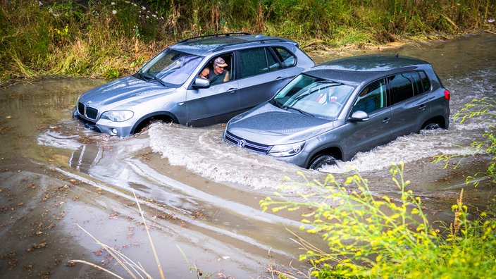 Zwei Autos stecken in Hochwasser fest, die Fahrer unterhalten sich aus ihren Fenstern.