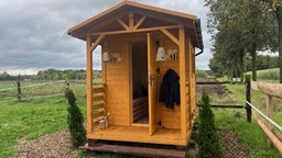 Ein kleines Holzhaus steht auf einer umzäunten Wiese