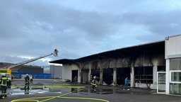 Eine ausgebrannte Halle vor der Einsatzkräfte der Feuerwehr arbeiten