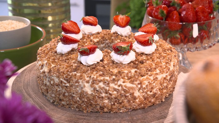 Der Frankfurter Kranz wird auf einer Holzplatte serviert, im Hintergrund Erdbeeren