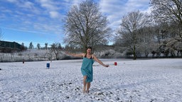 Eine Frau im Badeanzug mit einem Handtuch bekleidet auf einer Schnee bedeckten Wiese im Freibad