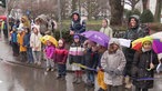 Teilnehmende Kinder mit Reckenschirmen am Straßenrand. 