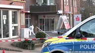 Zu sehen ist ein Absperrband und ein Polizeiauto vor dem Gebäude einer Sparkasse.