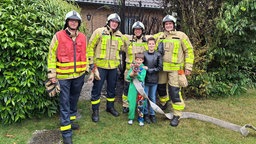 Vier Feuerwehrmänner und zwei Jungen vor einer verbrannten Hecke.