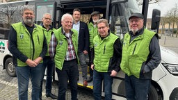 Eine Gruppe von Männern in grünen Westen steht vor einem Kleinbus