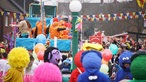 Ein Karnevalswagen mit orange kostümierten Jecken fährt am Nelkendienstag durch Olfen, viele kostümierte Besucherinnen und Besucherinnen stehen am Straßenrand.