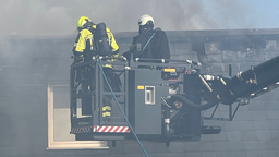 Feuerwehrmänner auf Feuerwehrdrehleiter vor brennendem Haus