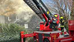 Feuerwehrmänner mit Feuerwehrfahrzeug vor rauchendem Haus