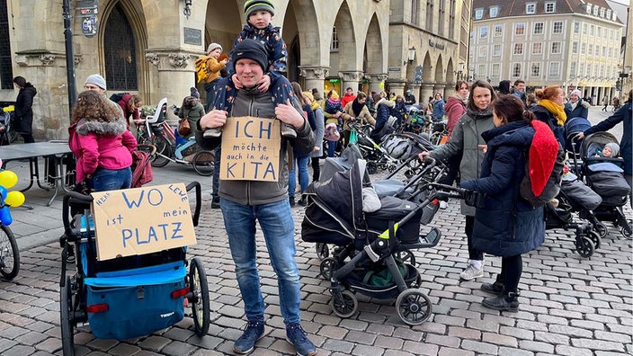 Eltern demonstrieren mit ihren Kindern auf der Straße für eine gerechtere Kita-Platzvergabe.