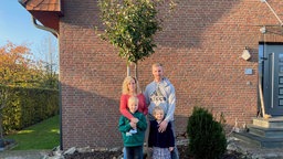 Familie steht vor frisch gepflanztem Apfelbaum 