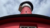 Ein roter Leuchtturm von unten fotografiert.