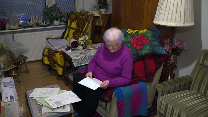 Ältere Dame in violetten Pulli liest auf dem Sofa ein Schriftstück