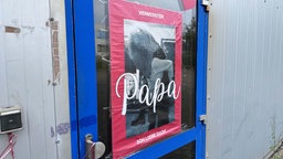 Ein rotes Plakat mit der Aufschrift "Vermisster Papa ich liebe dich!" hängt an der Tür einer Lagerhalle