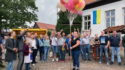 Frau hält einen Straus aus Luftballons in der Hand, um sie herum stehen viele Menschen