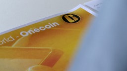 Auf einem weißen Tisch liegt ein Blatt Papier darauf gedruckt das Onecoin-Logo.