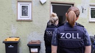 Zoll-Beamtinnen stehen vor einer geöffneten Haustür