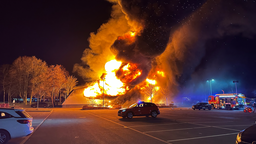 Ein Parkplatz mit lichterloh brennender Tennishalle im Hintergrund.