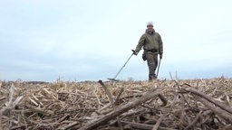 Ein Mann läuft mit einer Sonde über ein Feld.