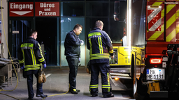 Ein rot-weißes Feuerwehrfahrzeug. Daneben stehen drei Männer. Sie tragen blau-neongelbe Feuerwehrkleidung.