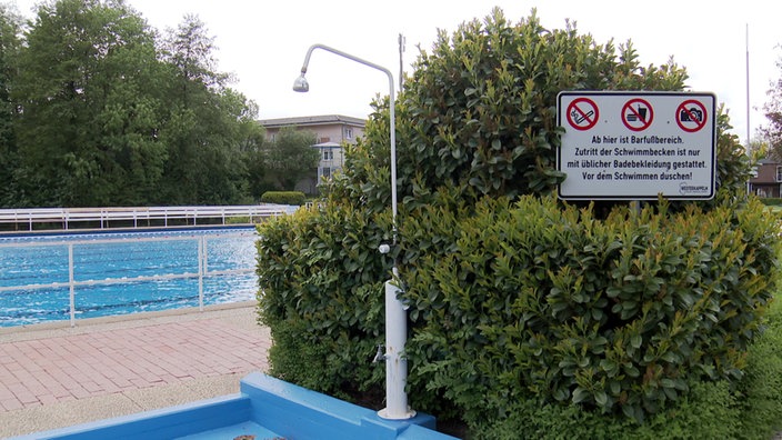 Bick auf das Freibadgelände in Westerkappeln mit Dusche, Schwimmbecken und einem Hinweisschild