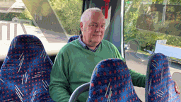 Ein Mann sitzt in der letzten Reihe eines Schulbusses und schaut in die Kamera