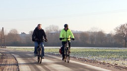 Zwei Fahrradfahrer fahren an einem Feld entlang.