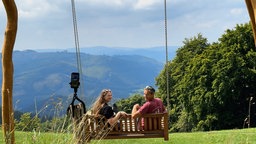 Zwei Besucher auf einer Schaukel in der Wildwiese.