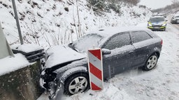 Ein Auto ist gegen eine Mauer gefahren, die Straße ist verschneit, im Hintergrund ein Polizeiauto