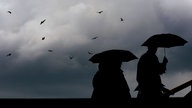 Passanten gehen mit Regenschirmen in Köln durch die Stadt