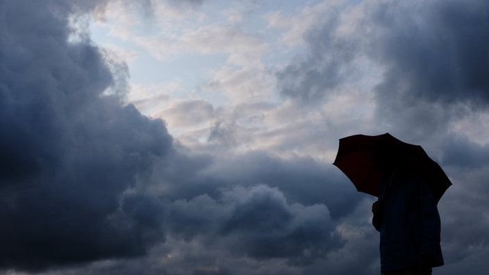 Ein Mann geht mit einem Regenschirm vor aufziehenden dunklen Wolken spazieren