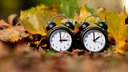 Zwei schwarze Uhr im Herbstlaub symbolisieren Zeitumstellung