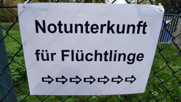 Papierschild mit der Aufschrift "Notunterkunft" an einem Maschendrahtzaun