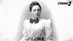 Emmy Noether ist auf dem schwarz-weiss-Bild zu sehen. Sie schaut seitlich an der Kamera vorbei. 