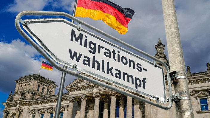 Ein weisses Hinweisschild mit der Aufschrift "Migrationswahlkampf" an einem Laternenmast vor dem Berliner Reichstagsgebäude