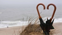 Regenschirme nebeneinander bilden Herz aus ihren Griffen, Strand Nordsee, Sylt.