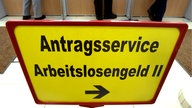 Kunden einer Arbeitsagentur stehen hinter einem Schild mit der Aufschrift "Antragsservice Arbeitslosengeld II" an verschiedenen Serviceschaltern