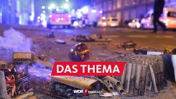 Abgebrannte Böller liegen nach der Silvesternacht auf der Straße, im Hintergrund stehen Einsatzkräfte der Feuerwehr