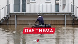 Ein Mann sitzt in einem Schlauchboot und paddelt zu einem Haus, das im Wasser steht.