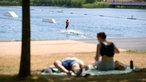 Wasserski-Fahrer ist auf einem See unterwegs, während Ausflügler die Sonne genießen