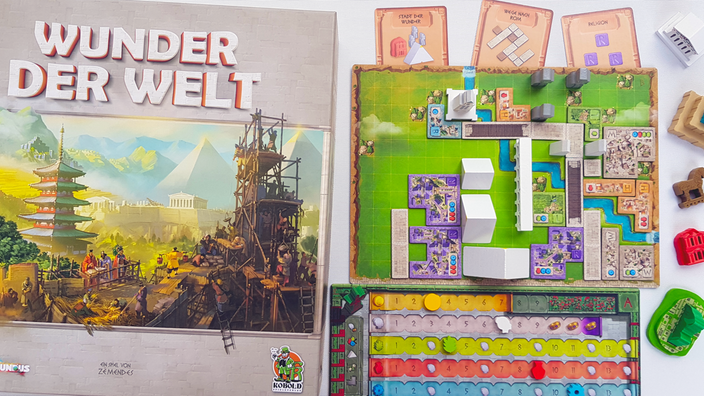 Die Spieleschachtel von "Wunder der Welt" zeigt Arbeiter auf einer antiken Baustelle, daneben ein Spielplan mit bunten Stadtteilen und dreidimensionalen hölzernen Gebäuden