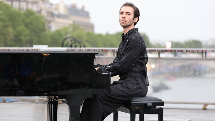 Pianist Alexandre Kantorow sitzt auf einem Podest an einem Fluss am Flügel