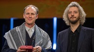 Der Filmemacher Ben Russell (l) mit einem Palästinensertuch auf die Bühne. Er äußerte Genozid-Vorwürfe wegen des israelischen Vorgehens im Gazastreifen. Aus dem Publikum kam Applaus.