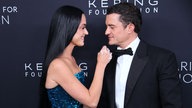 Katy Perry im blauen Abendkleid bewegt ihre Hand zu Orlando Bloom. Beide schauen und lächeln sich am 10.09.2024 an.