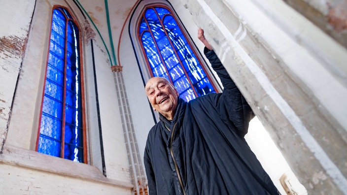 Der Künstler Günther Uecker steht im Schweriner Dom unter zwei der vier von ihm geschaffenen Kirchenfenster, die am Sonntag den 01. Dezember in einem Festakt der Öffentlichkeit vorgestellt wurden.