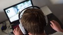  Ein Jugendlicher sitzt mit einem Headset vor einem Laptop und spielt ein Online-Computerspiel.