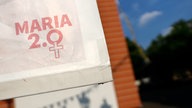 Ein Schild der Aktion Maria 2.0 hängt vor einer Kirche.